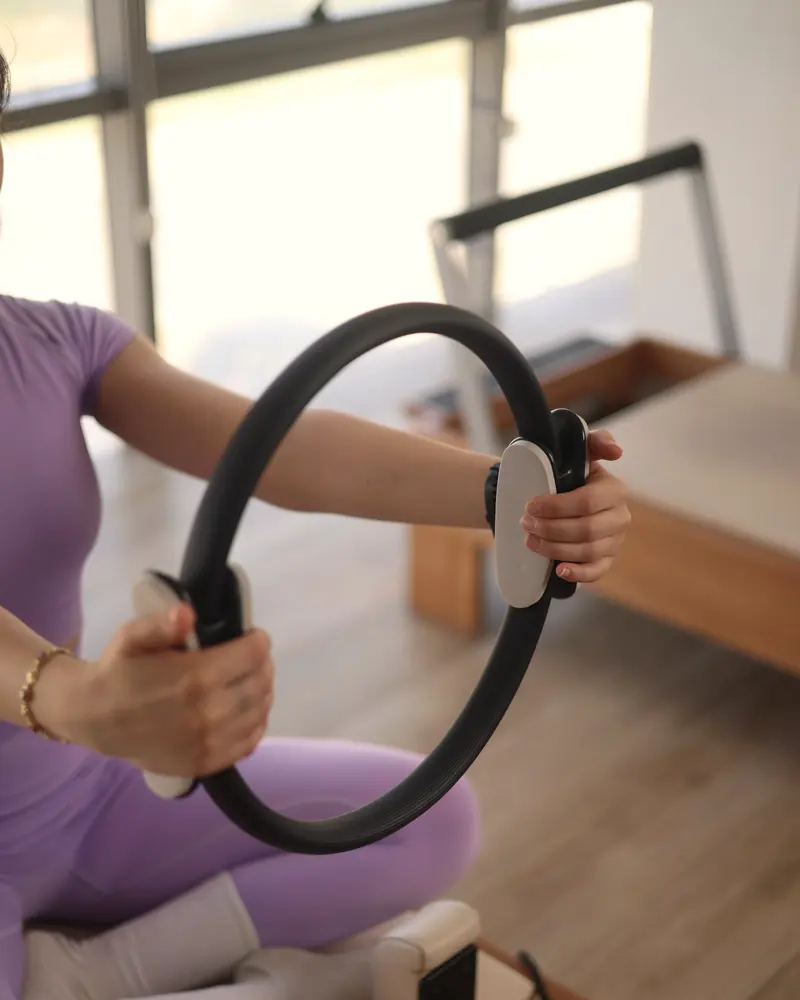 Eine Frau hält einen Pilates-Ring mit beiden Händen vor dem Körper und drückt ihn zusammen.